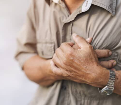 Close-up of an elderly man's hand held his chest in pain. Concept of heart disease.