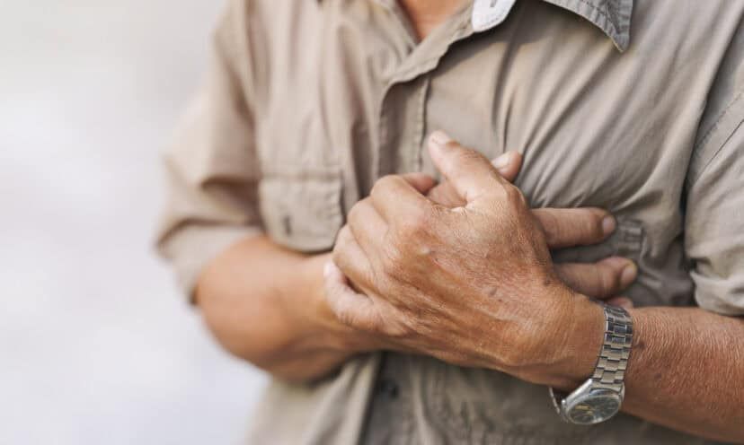 Close-up of an elderly man's hand held his chest in pain. Concept of heart disease.