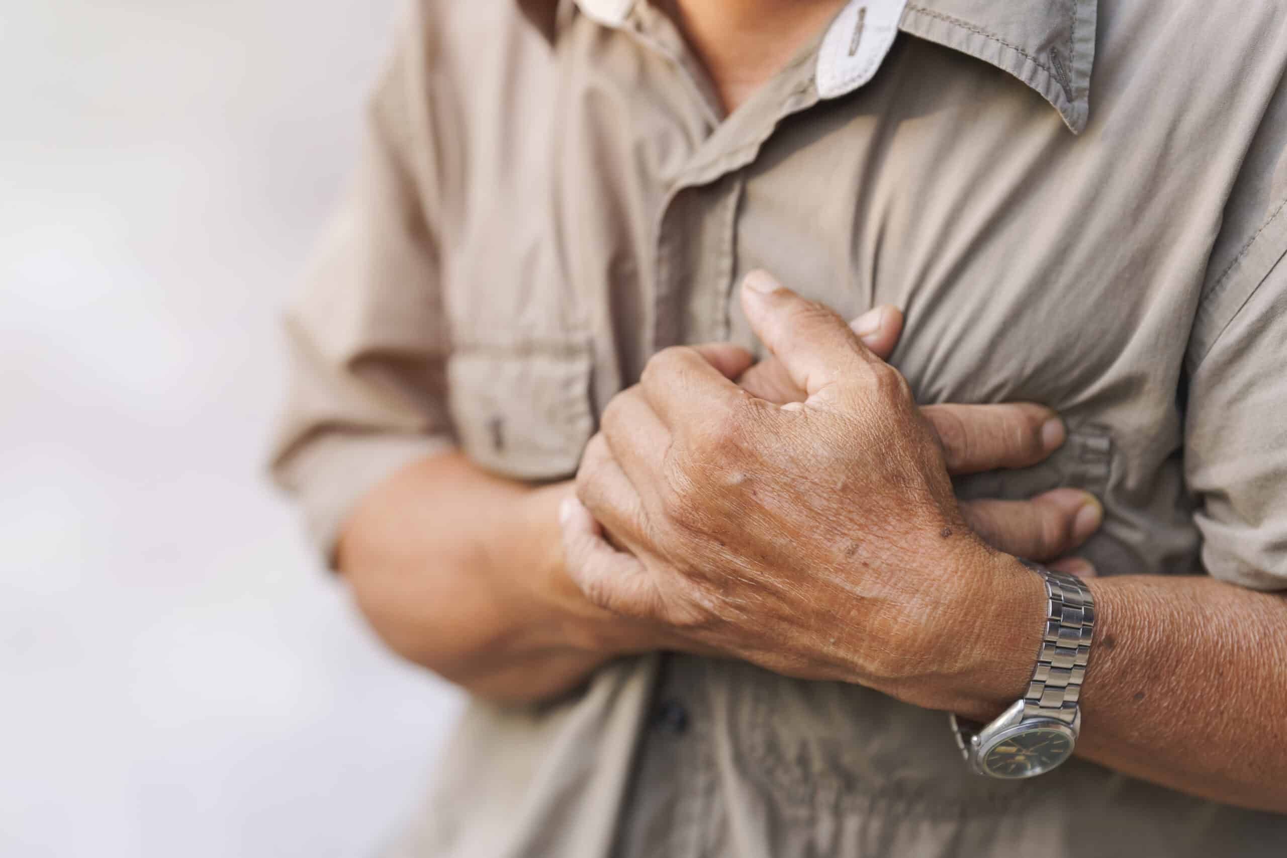 Close-up of an elderly man's hand held his chest in pain. Concept of heart disease.