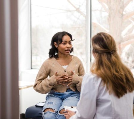 Young adult female patient gestures while explaining her mental health struggles with the doctor