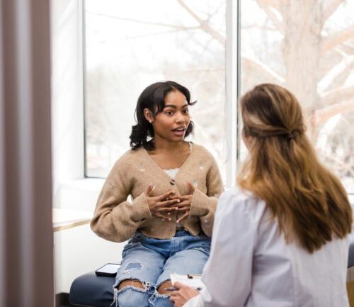 Young adult female patient gestures while explaining her mental health struggles with the doctor