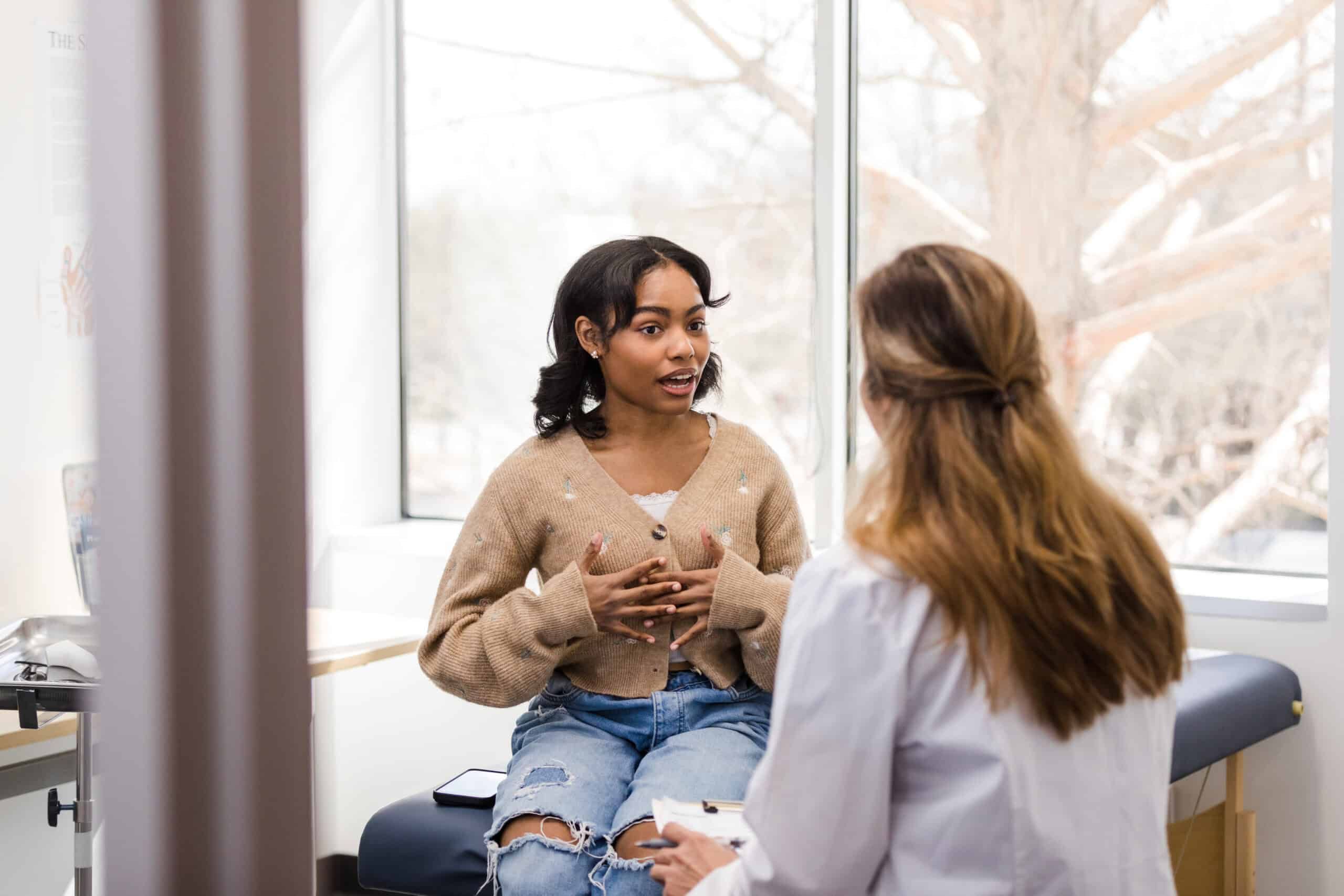 Young adult female patient gestures while explaining her mental health struggles with the doctor
