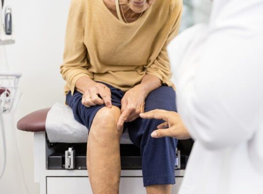 Woman sitting in patient room showing doctor where her knee hurts