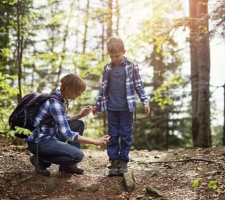 Mother and son hiking in forest. Mother is applying tick repellent on the son's legs.