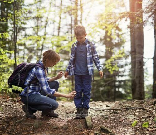 Mother and son hiking in forest. Mother is applying tick repellent on the son's legs.