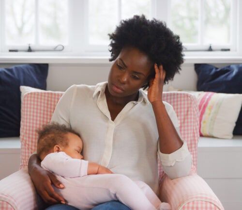 New Mother Suffering With Post Natal Depression Holding Sleeping Baby Daughter In Nursery At Home