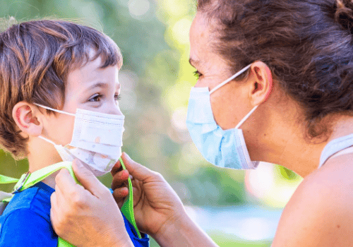 A mother adjusts her son's face mask