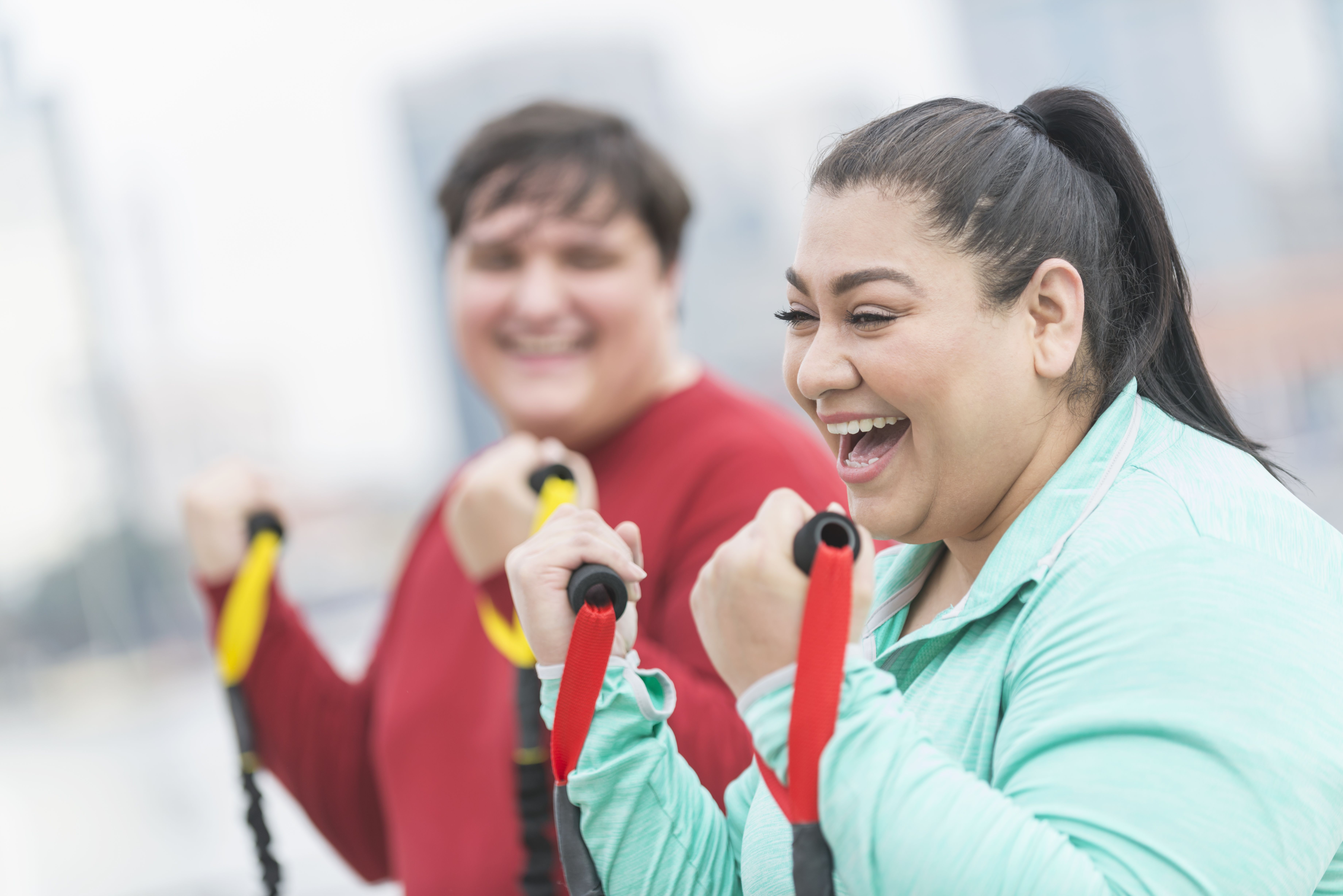 Hispanic woman, friend exercising with resistance bands