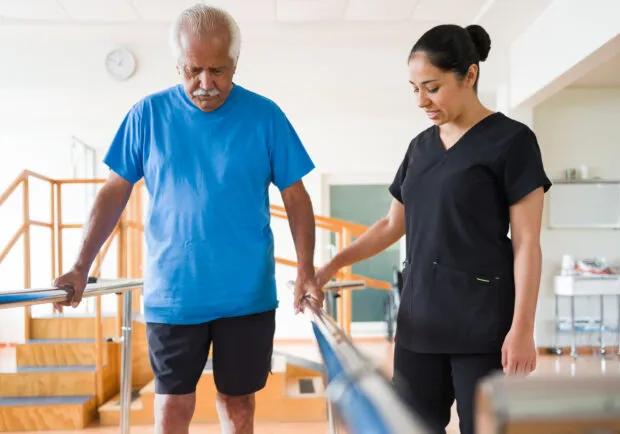 Senior man giving small steps between parallel bars