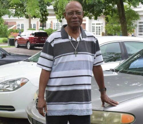 Patient Darryl stands in the parking lot, touching his car