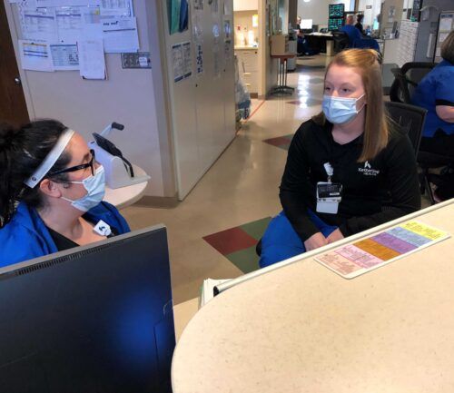 Young nurse sits with coworker talking with masks