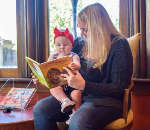 Woman participates in the Dolly Parton Imagination Library and reads a book to a baby sitting on her lap