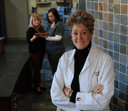 Dr. Peterson stands with arms cross, two women stand behind her