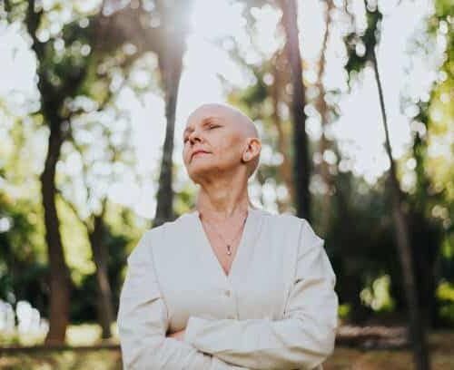 Woman with cancer in a white sweater standing in the forest