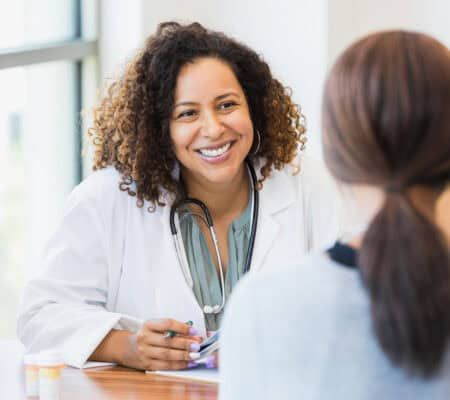 A smiling mid adult female doctor listens as a female patient discusses her health.