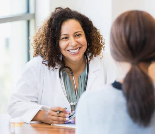 A smiling mid adult female doctor listens as a female patient discusses her health.