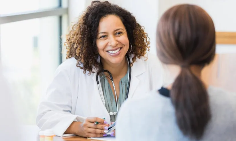 A smiling mid adult female doctor listens as a female patient discusses her health.