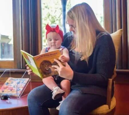 Woman participates in the Dolly Parton Imagination Library and reads a book to a baby sitting on her lap