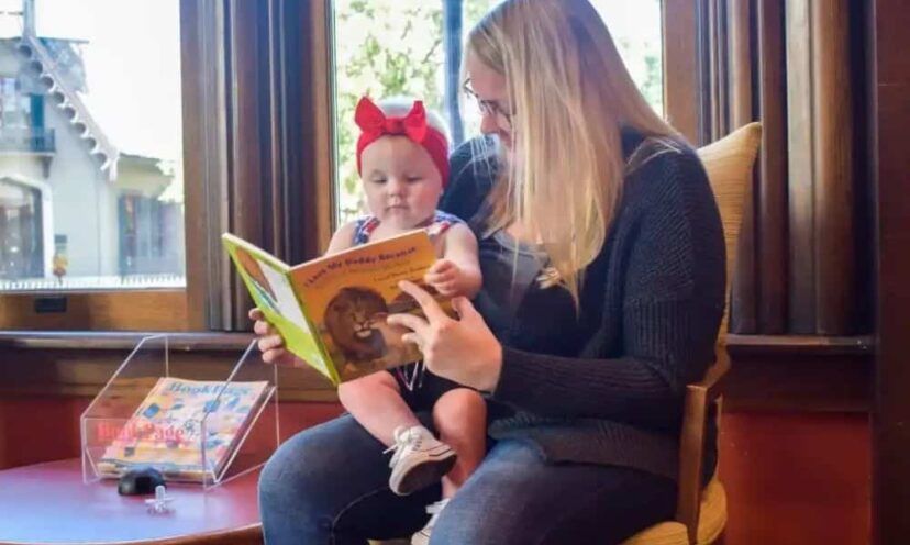Woman participates in the Dolly Parton Imagination Library and reads a book to a baby sitting on her lap