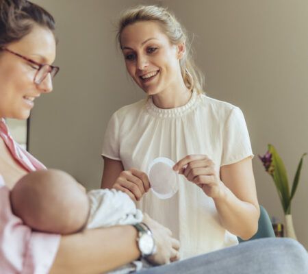Mom breastfeeding while woman shows her a breast pad