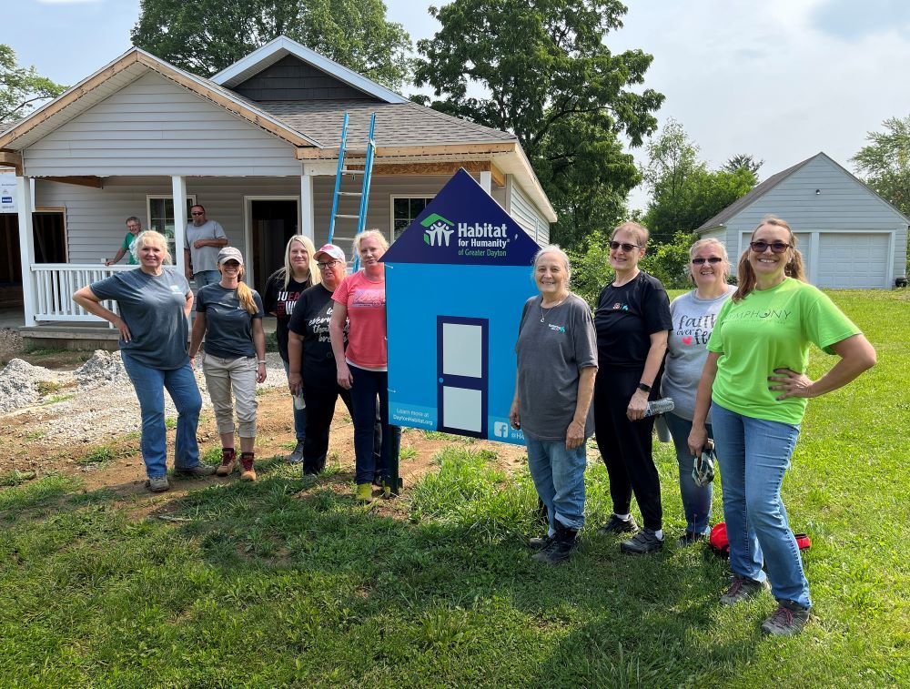 Women in IT standing in front of a house with a habitat for humanity sign