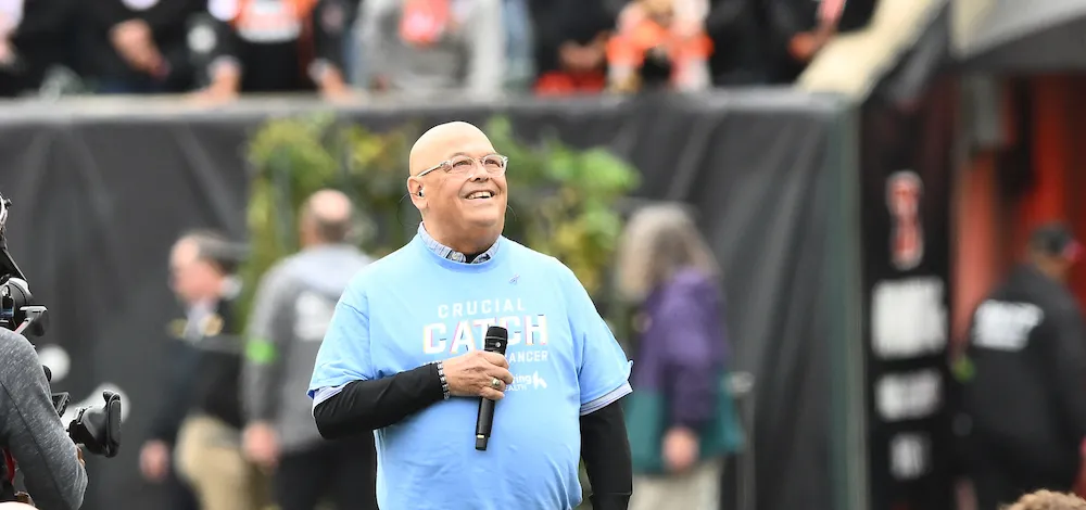 Tom Beery holds a microphone on the field at Paycor Stadium, where he sang the National Anthem.