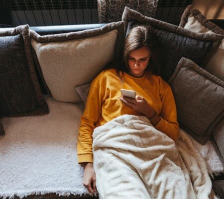 Woman sitting alone on couch looking at her phone.