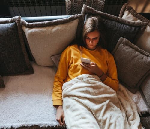 Woman sitting alone on couch looking at her phone.