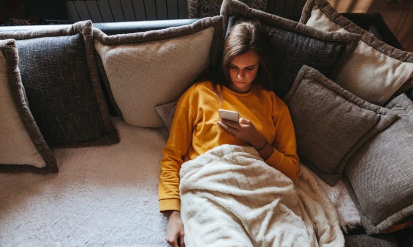 Woman sitting alone on couch looking at her phone.