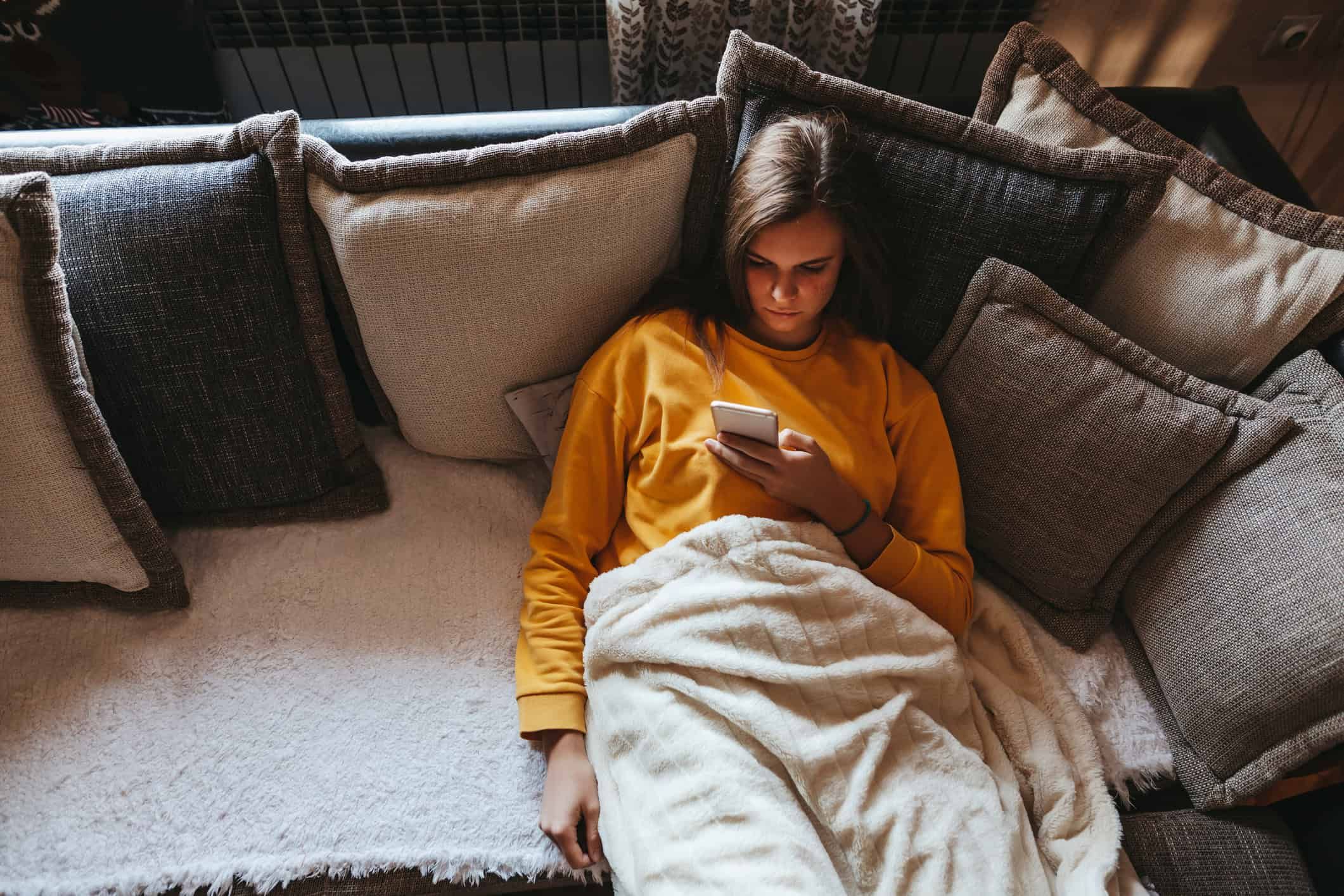 Woman sitting alone on couch looking at her phone.