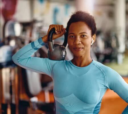 Black female athlete with kettlebell in a gym looking at camera.