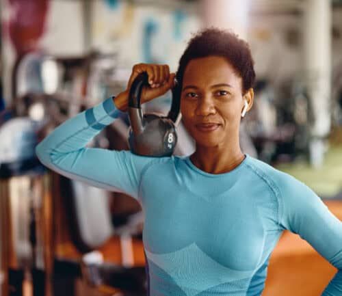 Black female athlete with kettlebell in a gym looking at camera.