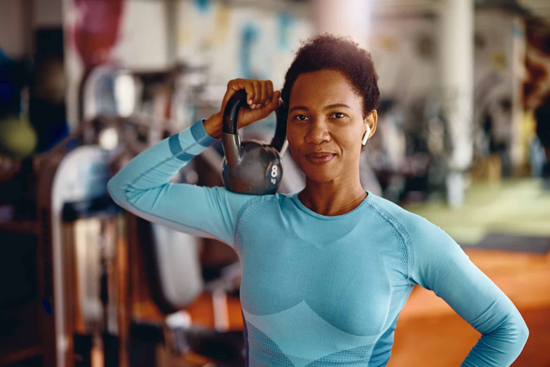 Black female athlete with kettlebell in a gym looking at camera.