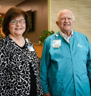 Susan Riegel and Chuck the volunteer stand at the front desk of Kettering Health Miamisburg, greeting guests.