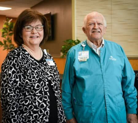 Susan Riegel and Chuck the volunteer stand at the front desk of Kettering Health Miamisburg, greeting guests.