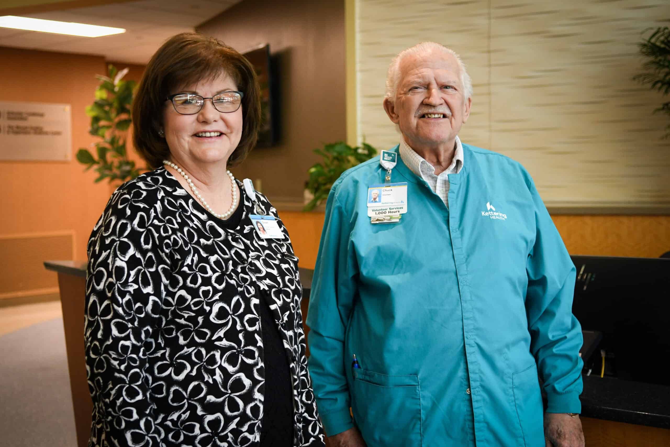 Susan Riegel and Chuck the volunteer stand at the front desk of Kettering Health Miamisburg, greeting guests.