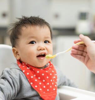 Baby eating baby food in a high chair.