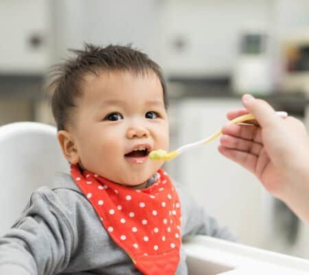 Baby eating baby food in a high chair.