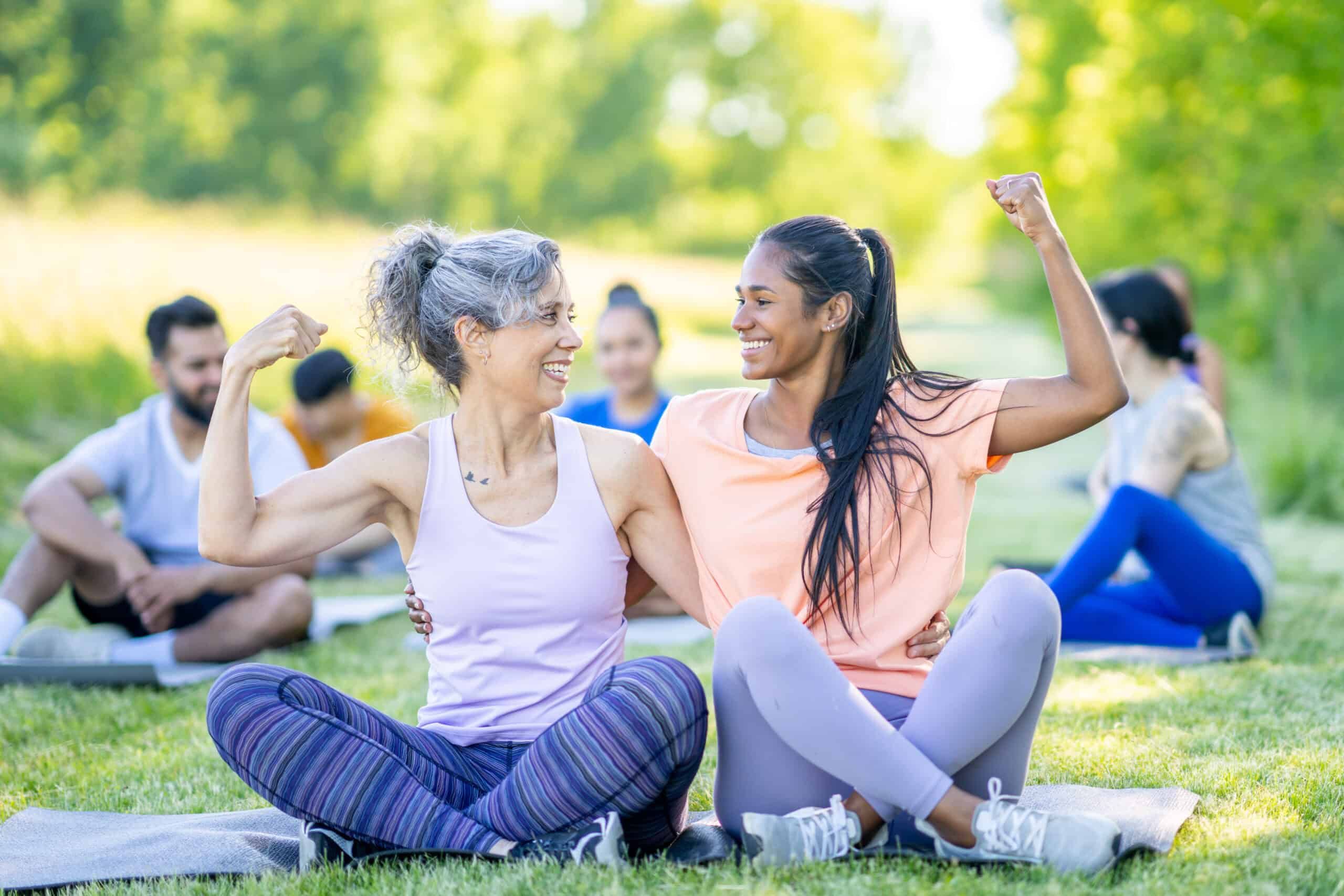 older woman and younger woman sitting outside, flexing their biceps