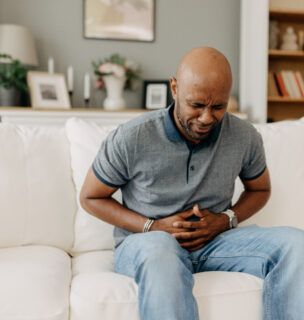Man suffering from stomach pain on white couch indoors