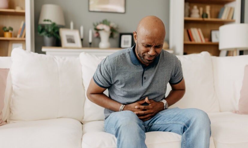Man suffering from stomach pain on white couch indoors