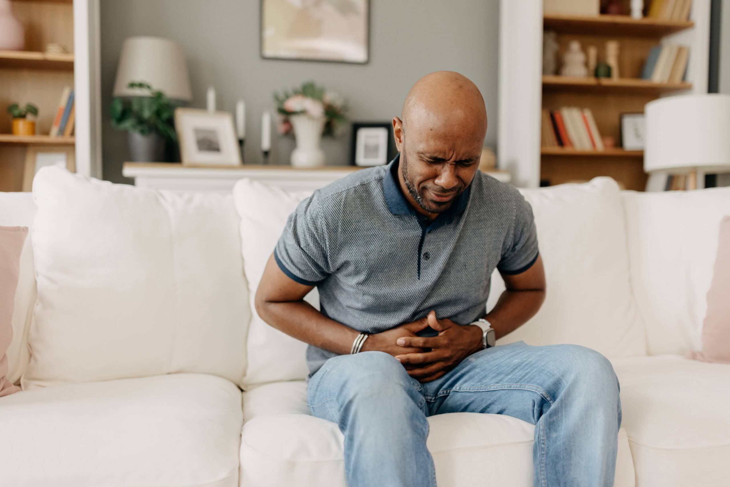 Man suffering from stomach pain on white couch indoors