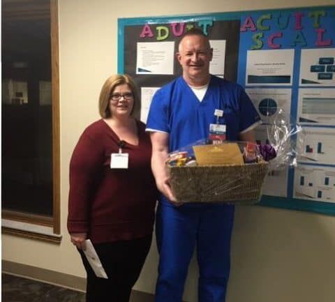 Two healthcare employees posing together, one holding gift basket in hospital hallway
