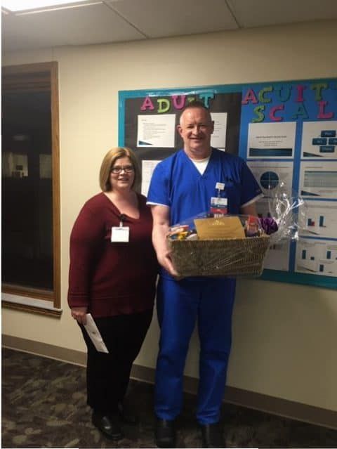 Two healthcare employees posing together, one holding gift basket in hospital hallway