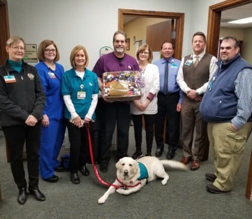 Group of healthcare employees posing with service dog and presentation basket