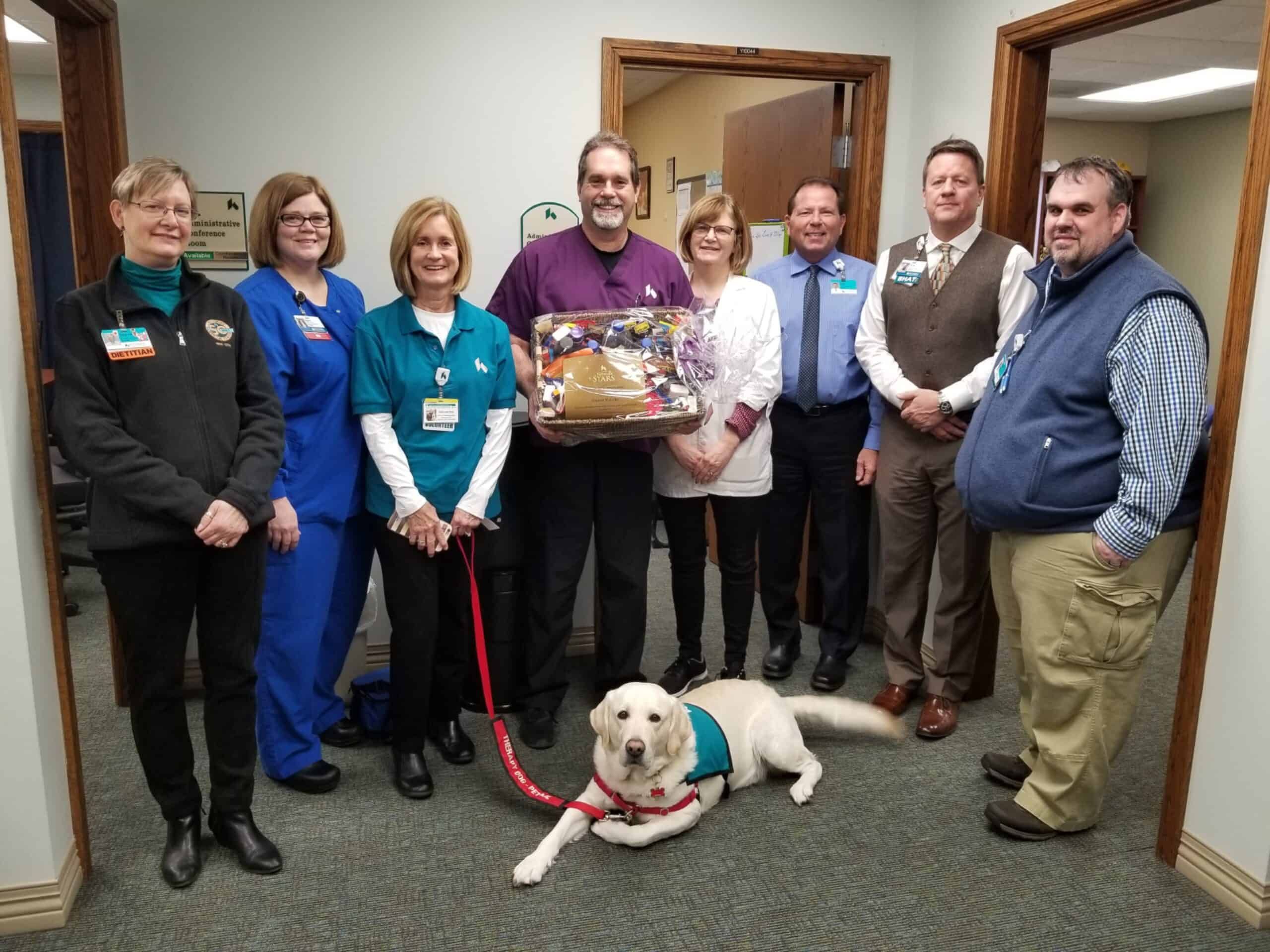 Group of healthcare employees posing with service dog and presentation basket