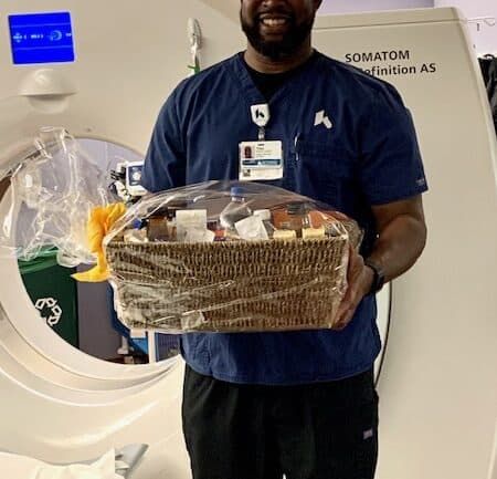 Healthcare worker holding gift basket standing next to Siemens medical imaging equipment