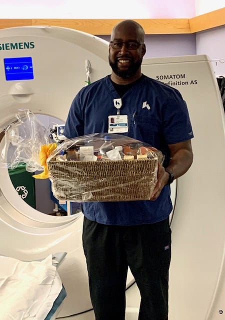 Healthcare worker holding gift basket standing next to Siemens medical imaging equipment