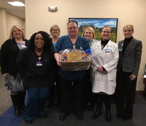 Group of healthcare staff members presenting gift basket to male colleague in scrubs