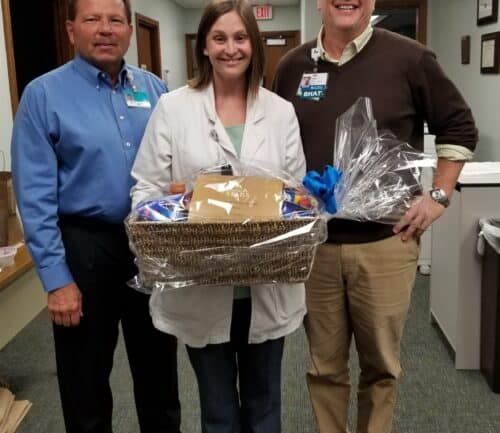 Three healthcare professionals presenting gift basket to employee recognition recipient